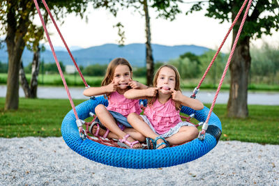 Portrait of twin sisters on swing at playground