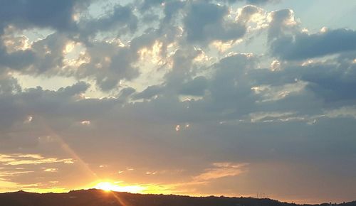 Low angle view of sunlight streaming through clouds during sunset