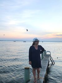 Full length of woman standing on pier in sea against sky during sunset