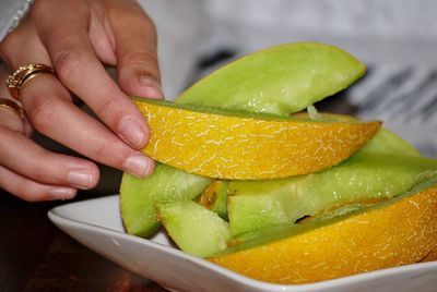 Cropped hand of woman picking fruit slice from plate