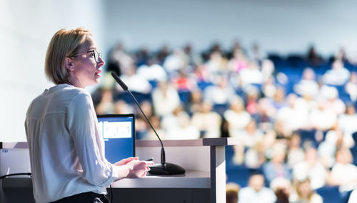 Female speaker giving a talk on corporate business conference. unrecognizable people in audience at