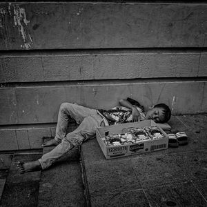Man sleeping on footpath against wall in city