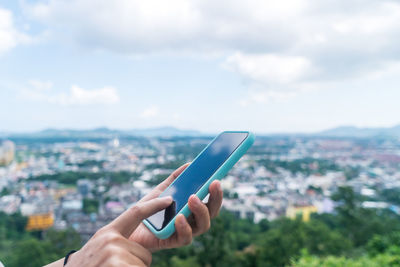 Midsection of person holding mobile phone against cityscape