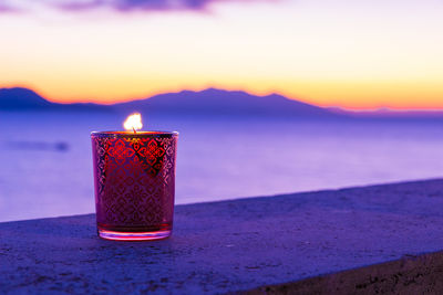 Close-up of illuminated tea light on table against sky during sunset