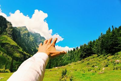 Cropped hand of man gesturing against blue sky