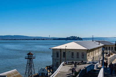 Buildings by sea against clear blue sky