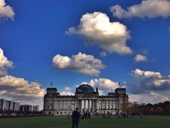 People in front of building against cloudy sky