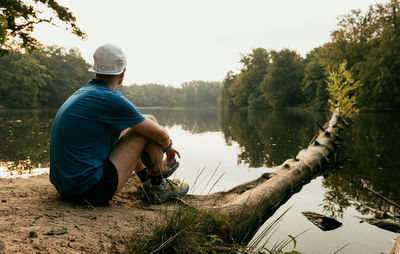 Man sitting by lake against trees