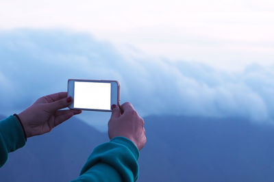 Cropped image of woman photographing against cloudy sky