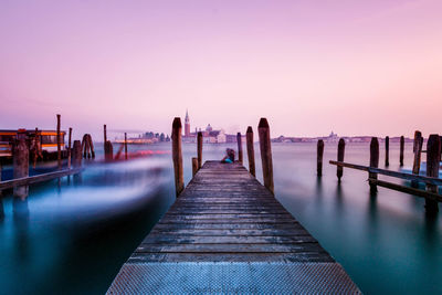 Pier over river against sky during sunset