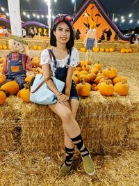 Full length portrait of a smiling young woman standing by pumpkins