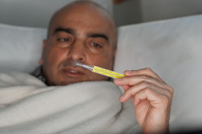 Man checking temperature while lying on bed at home