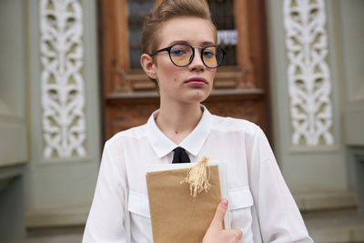 Portrait of young woman holding book standing outdoors