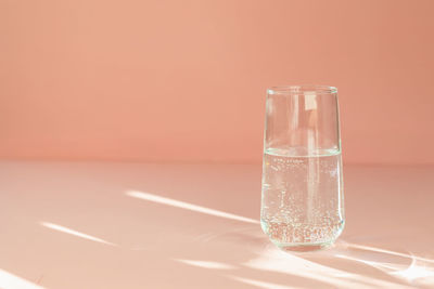 Transparent glass on a peach background in the sunlight gives