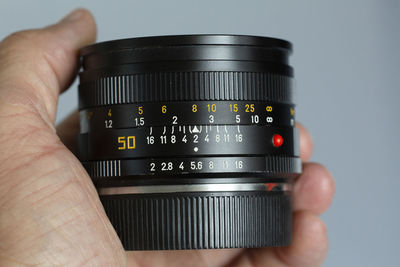 Close-up of hand holding camera lens against gray background