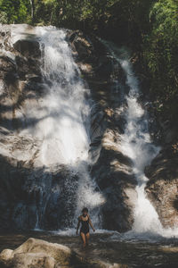 Full length of young woman splashing water in waterfall