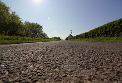 Surface level of road amidst trees on field against sky