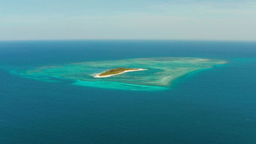 Small tropical island in the blue sea with a coral reef and the beach, top view. 