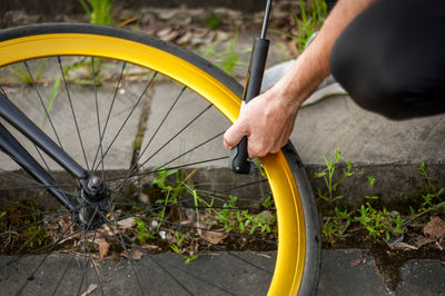 A young man pumps up the wheel of his bicycle. it does this by using a hand pump to pump air.