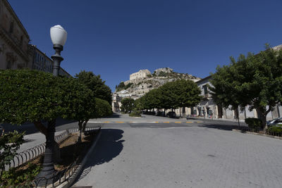 Street by trees against blue sky in scicli