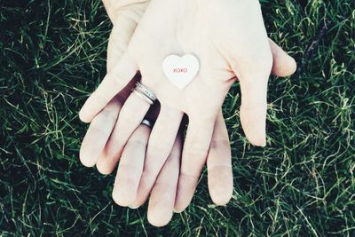 Cropped hands of people holding heart shape object over grass field