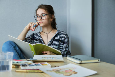 Millennial girl draws fabulous images on paper while sitting at home