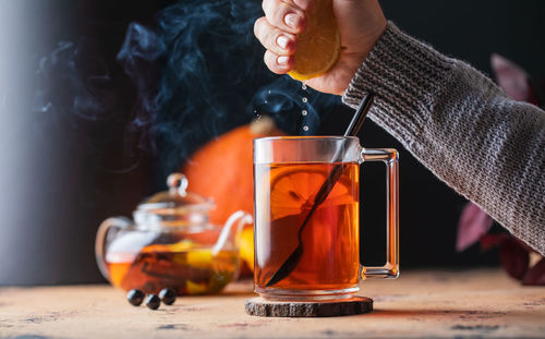 A woman's hand squeezes lemon juice into a mug of tea. autumn cozy composition.