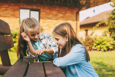 Two sisters laugh and play a wooden board game with colorful blue, red, green and yellow chips 