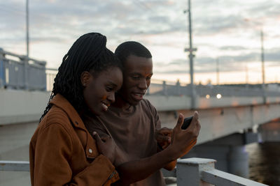 Boyfriend sharing mobile phone with girlfriend at bridge