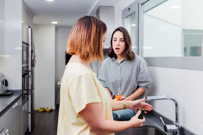 Woman washing cucumber at sink in kitchen