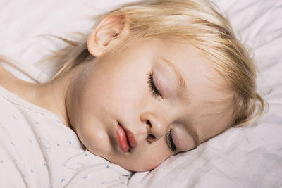 Little boy sleeping on white pillow. beautiful baby child with long blonde hair. close-up face. 