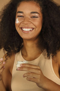 Portrait of smiling teenager girl applying moisturizer on face