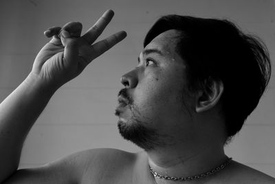 Close-up of serious man showing peace sign against wall