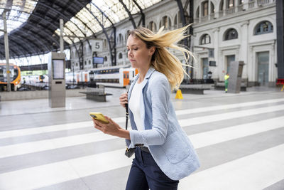 Businesswoman holding smart phone running at railroad station