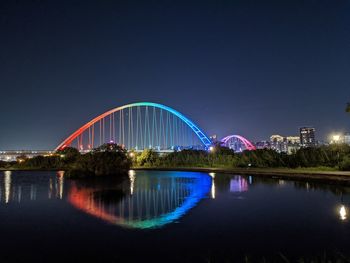 Illuminated bridge over lake against sky in city at night