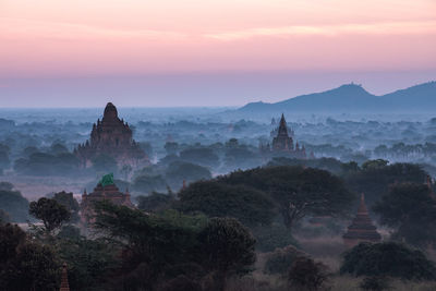 Temples against sky during sunrise in foggy weather