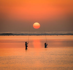 Silhouette people on beach against sky during sunset