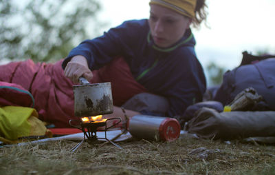 Female hiker making drink while leaning on bed at field during camping