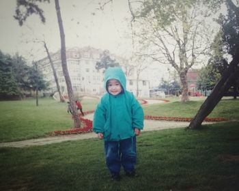 Portrait of boy standing on grass against trees