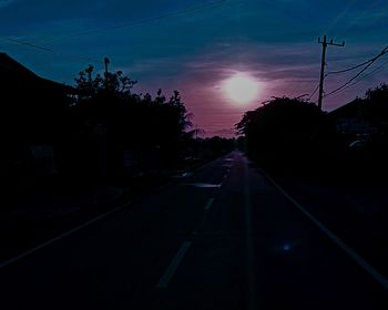 Road amidst silhouette city against sky during sunset