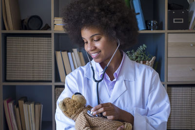 Smiling doctor examining stuffed toy at clinic