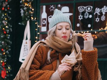 Young woman with blonde hair wearing brown fur coat eating sweet food on the christmas market. 
