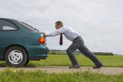 Side view of man standing by car on field
