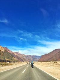 Rear view of people riding motorcycles on road leading towards mountains