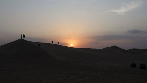 Silhouette people on desert against sky during sunset