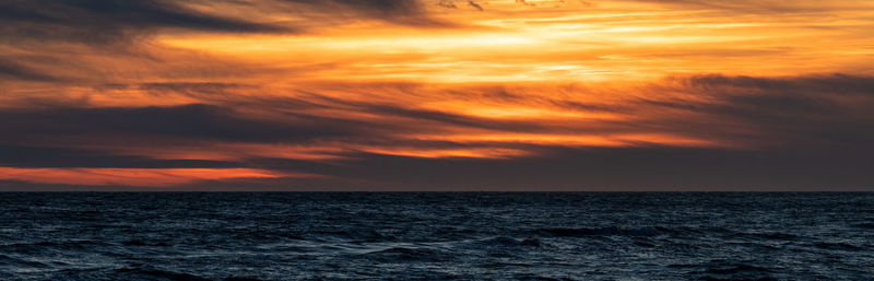 Scenic view of sea against dramatic sky during sunset