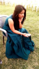 Young woman looking away while sitting on seat in field
