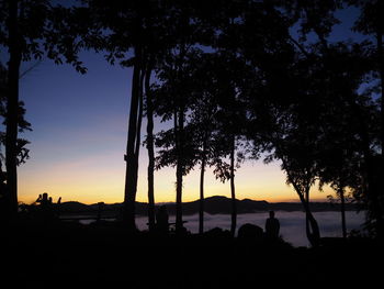 Silhouette trees by lake against sky during sunset