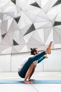 Side view of adult bearded man doing yoga firefly pose against wall with geometric ornament