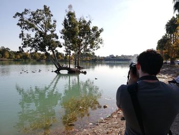 Rear view of man photographing lake against sky